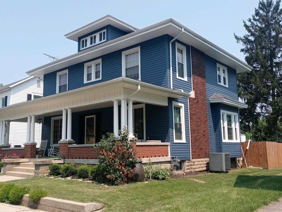 Blue two-story house with white trim, red brick porch, and a small front yard under a clear sky