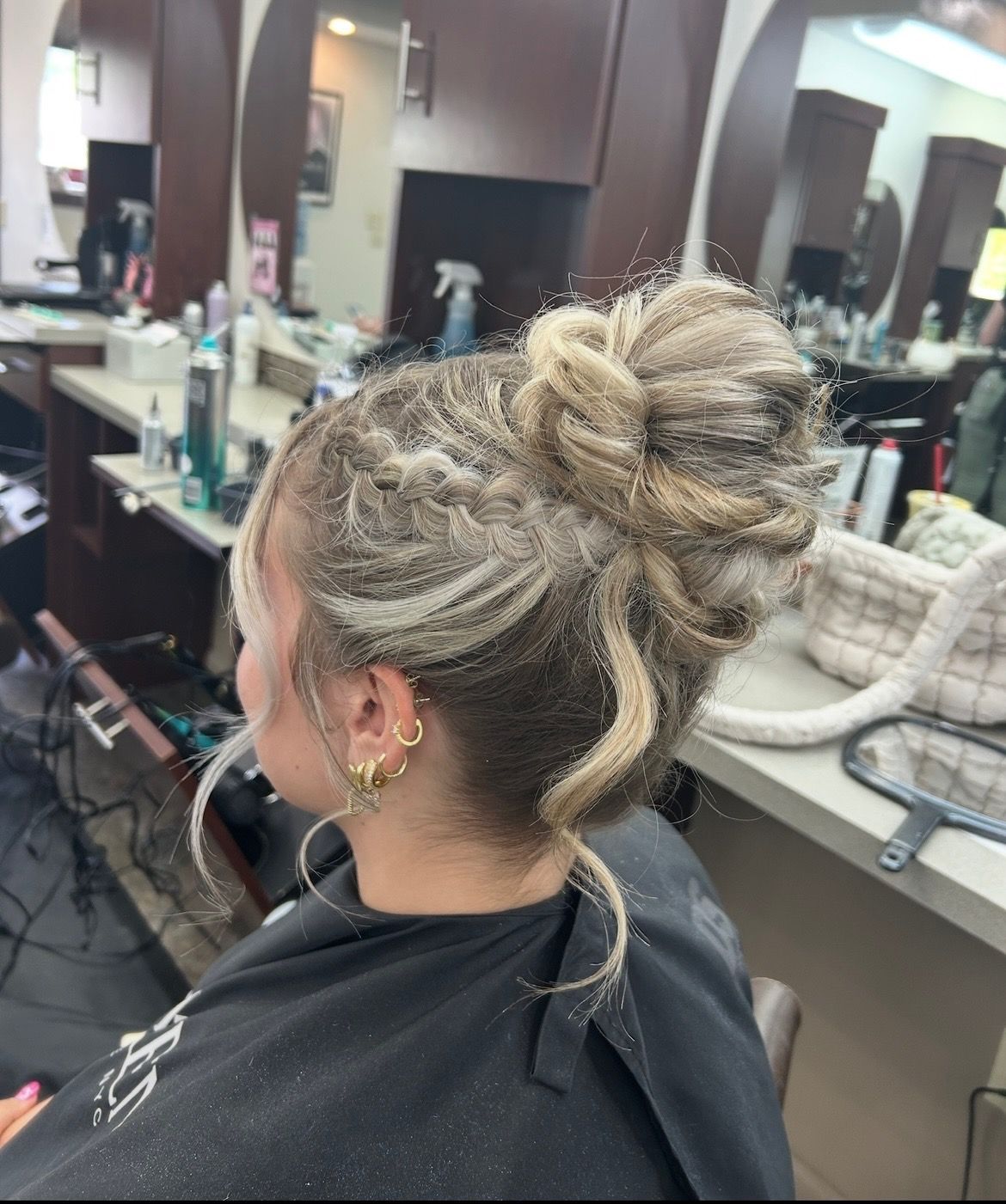 Woman with blonde updo in salon, hair styled with texture, wearing earrings.