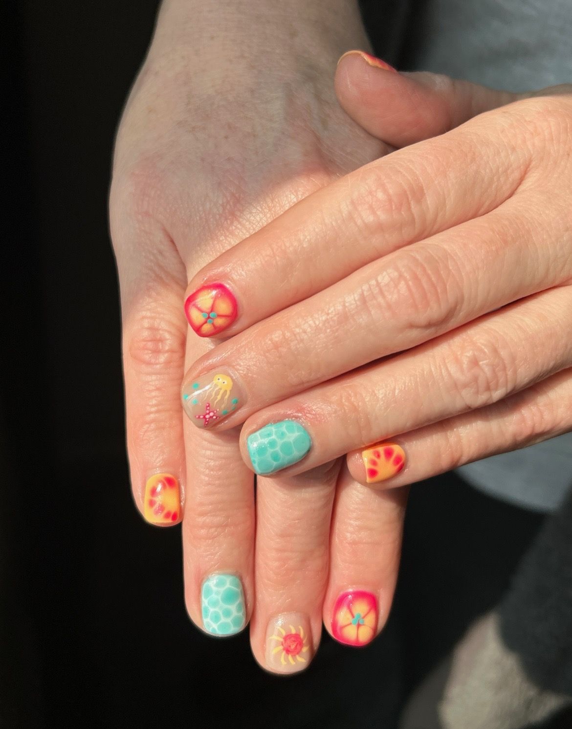 Hands with colorful nail art featuring floral and polka dot designs in orange, yellow, and teal.