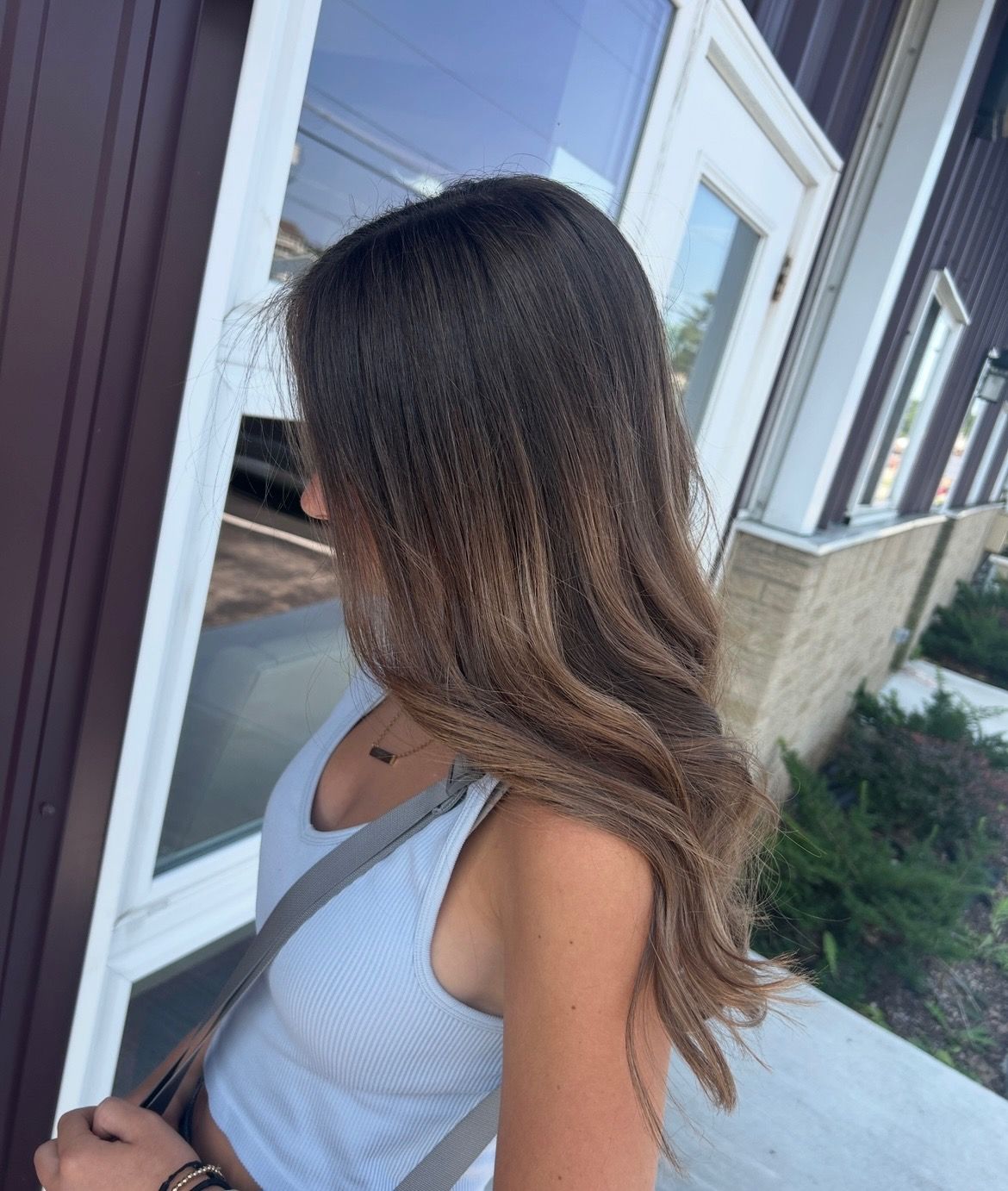 Woman with long brown ombre hair outside a building in a light blue top.