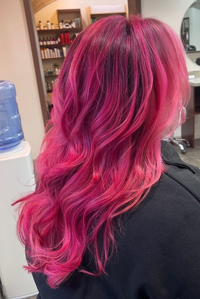 Woman with long, wavy, bright pink hair in a salon setting.