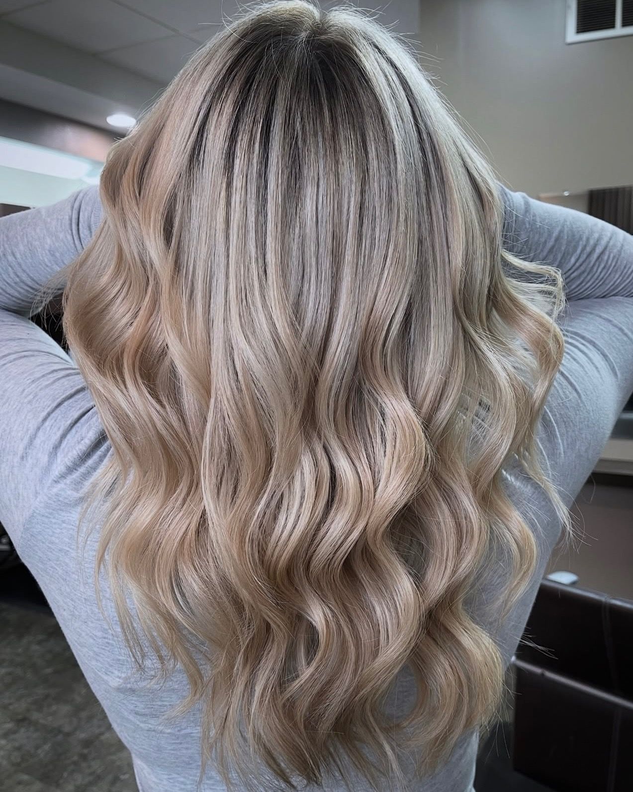 Woman with wavy, blonde hair, styled with dark roots.