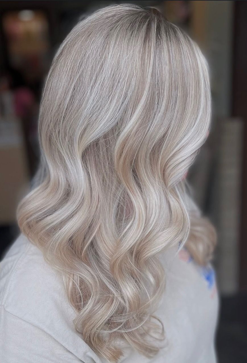 Woman with long, wavy, light blonde hair styled with a crimped texture, wearing a light-colored sweater.