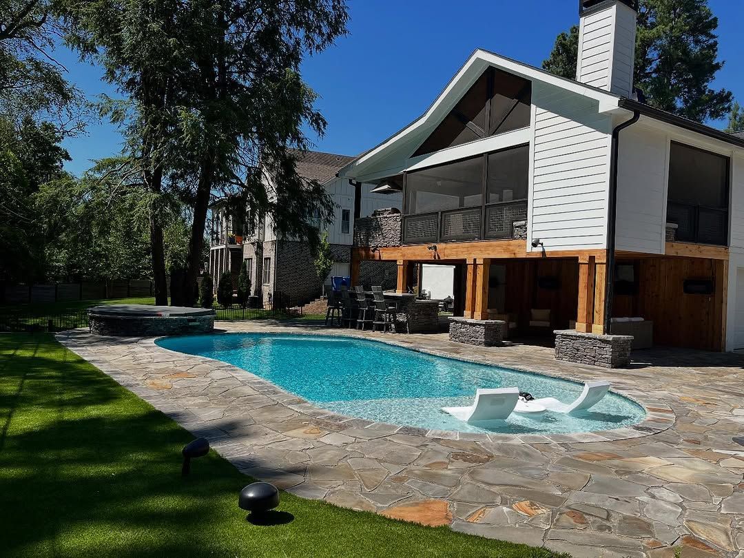 A large white house with a pool in the yard. The pool has a stone deck and lounge chairs in the water.