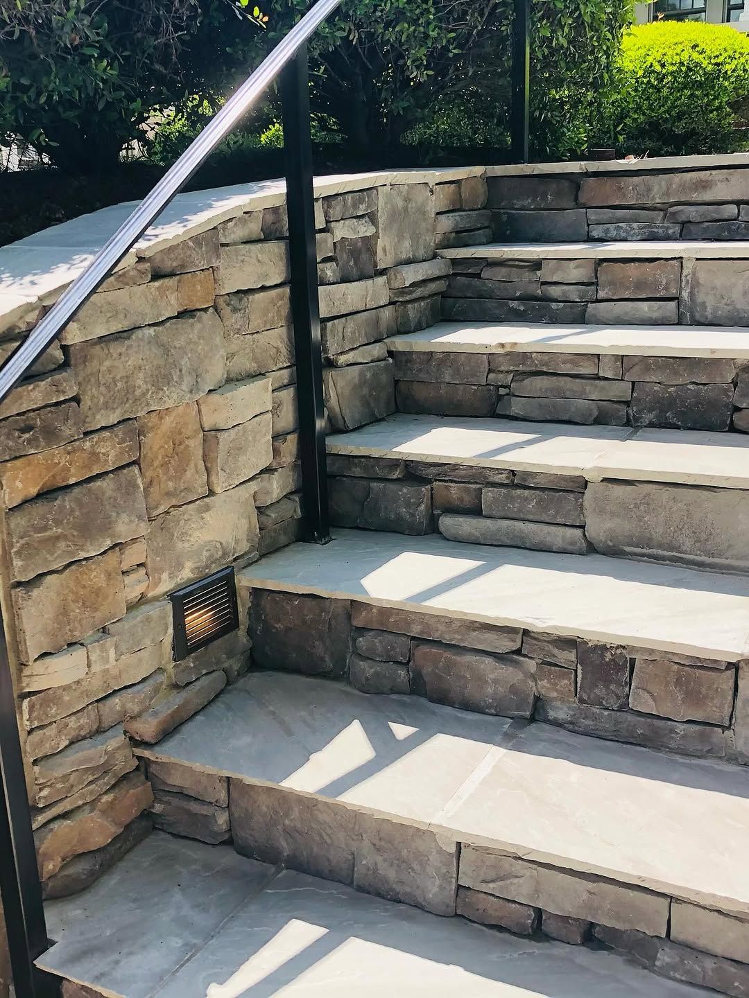 Stone steps with a metal handrail. A small light is in the stone wall.