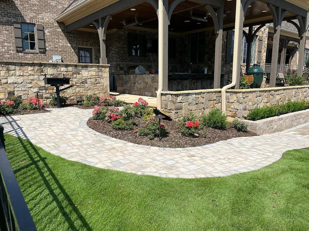 Stone pathway curves past a landscaped garden and covered patio attached to a brick home.