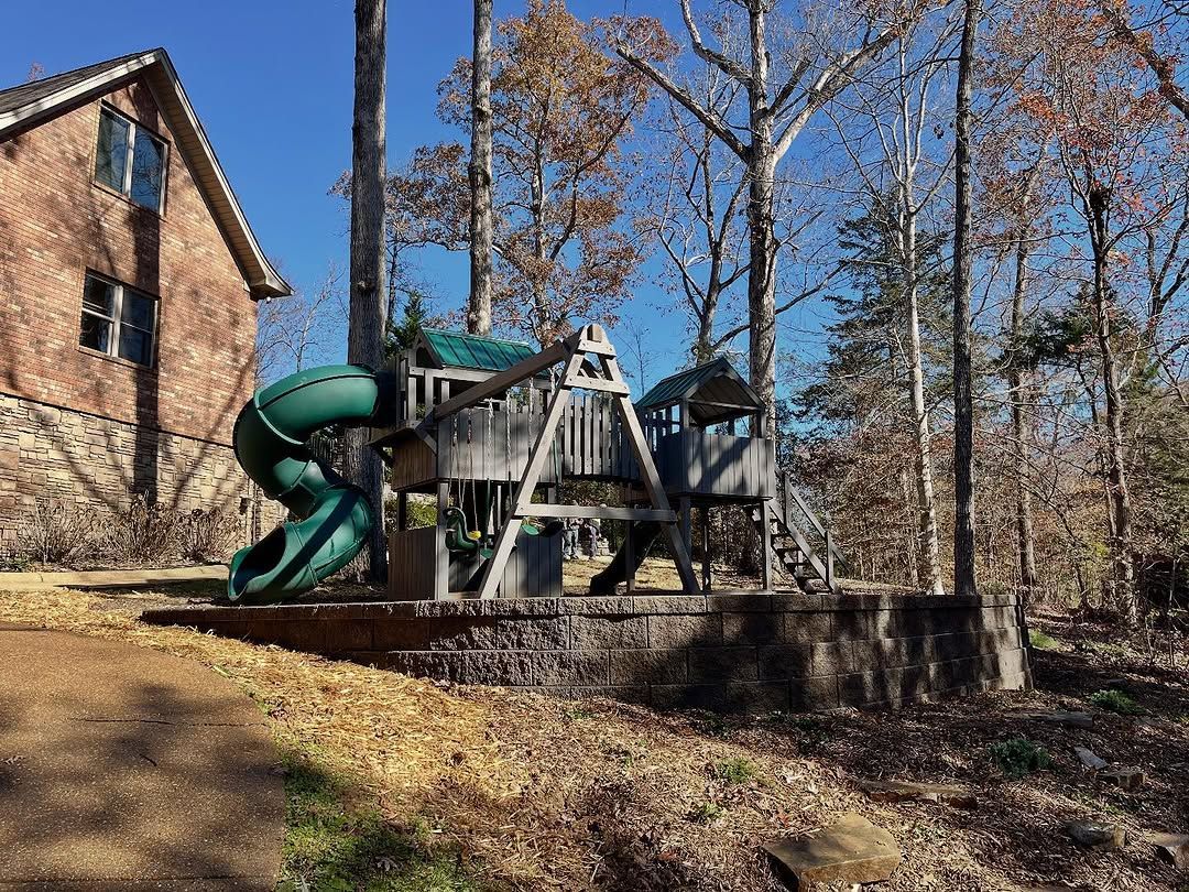 A green slide and wooden playset in a yard, near a brick house, on a sunny day.