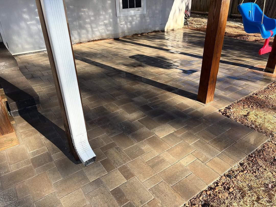 Patio paved with brown bricks next to a building and wooden structure.