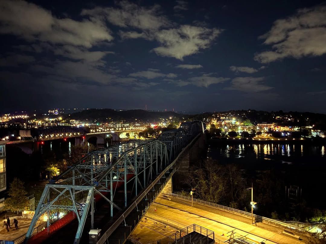 Night view of a bridge over a river, with city lights illuminating the dark sky and water.