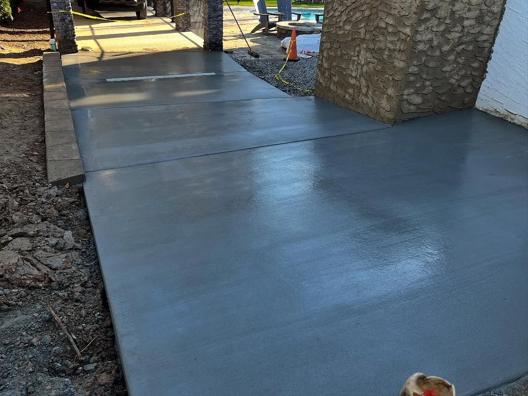Freshly poured concrete sidewalk, gray, next to a stone wall and dirt; sunlight reflecting.