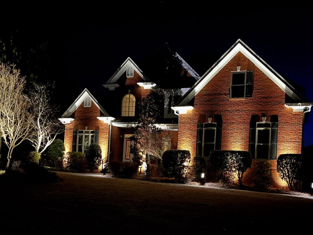 Brick house illuminated by landscape lighting at night.