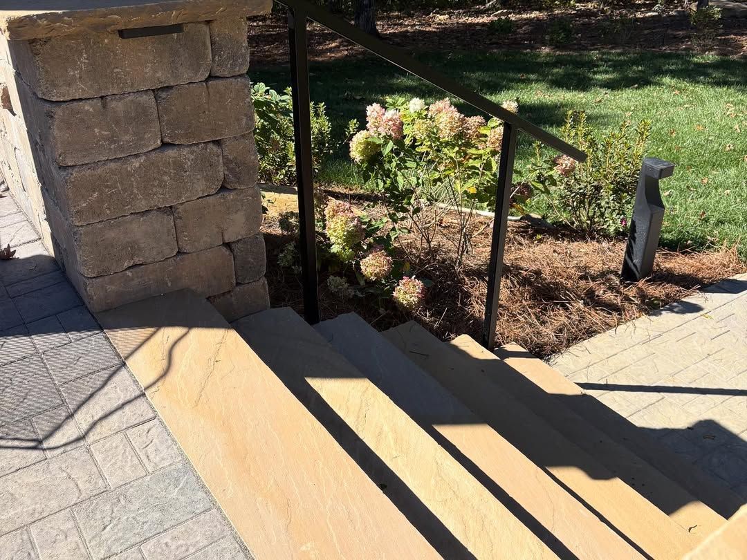 Stone staircase with handrail next to a stone pillar, leading to a garden.