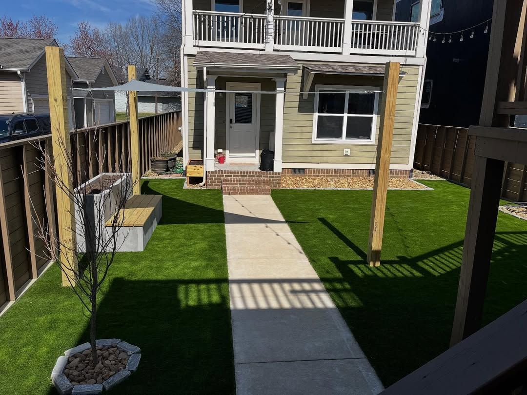 A two-story house with a small backyard, concrete path, and green artificial turf.