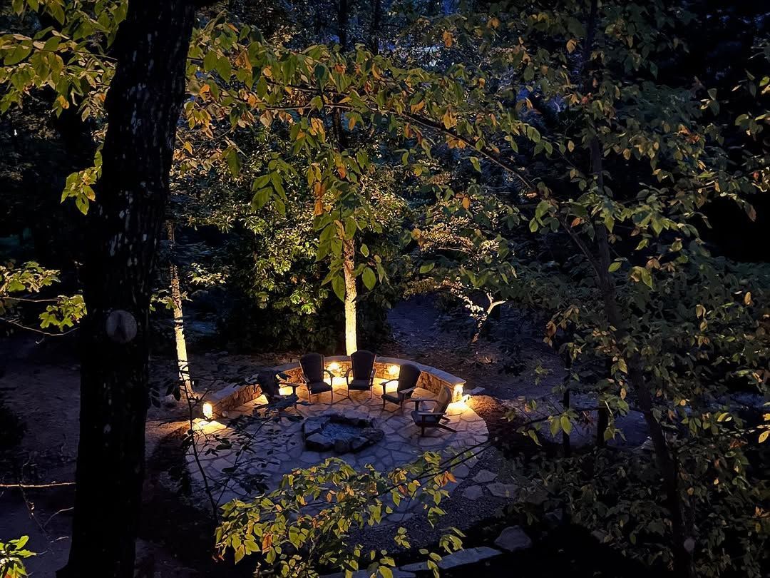 A cozy outdoor fire pit circle, illuminated at night, surrounded by trees.