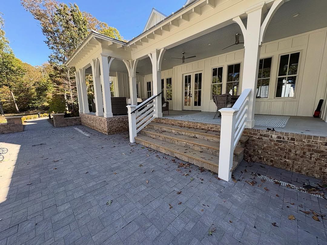 Covered porch with white columns and steps, brown stone accents, and paved patio.