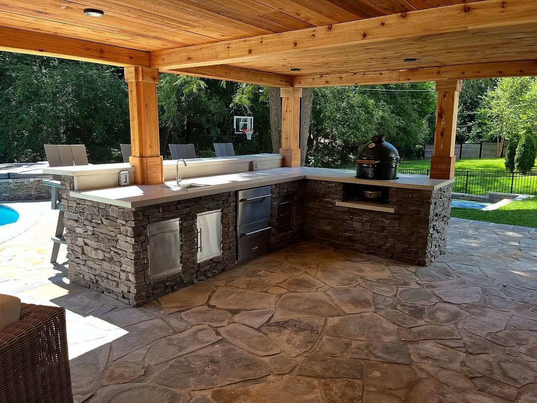Patio with stone floor, wooden beams, and built-in stone counter. Outdoor seating and pool visible in background.