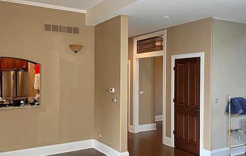 Empty beige room with hardwood floors, wall mirror, doorway, and a folding chair in the corner