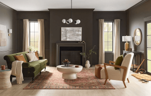 Cozy living room with dark walls, green sofa, white chairs, fireplace, rug, and large windows