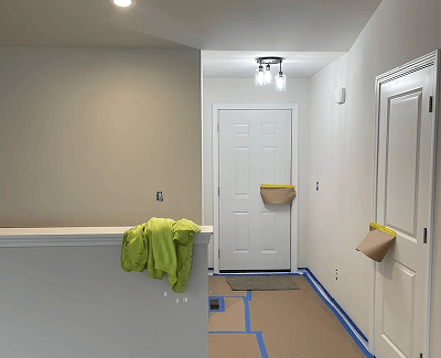 Hallway under renovation with taped floor, beige walls, and a green cloth draped over a half wall.