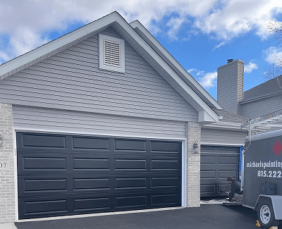 Gray house exterior with a black double garage door and blue sky above