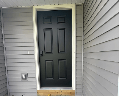 Black front door with six panels on a gray-sided house porch
