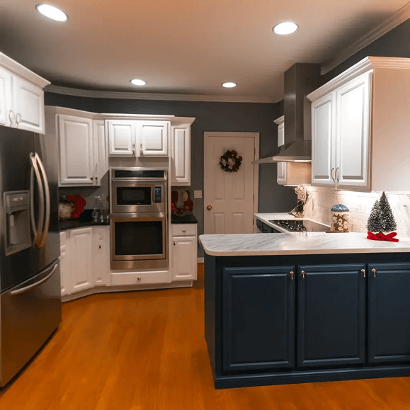 Modern kitchen with white cabinets, stainless steel appliances, dark blue island, and wood flooring