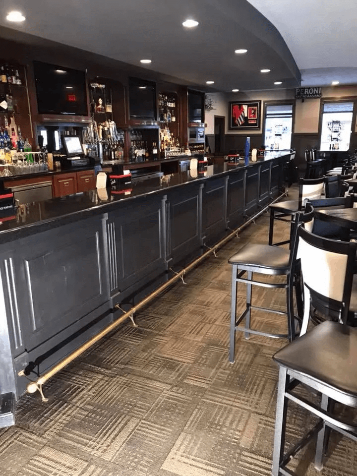 Empty bar interior with long counter, stools, dark wood shelves, and overhead lights