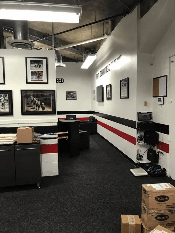 Empty office hallway with framed photos, black cabinets, white walls, and red-and-black stripe accents.