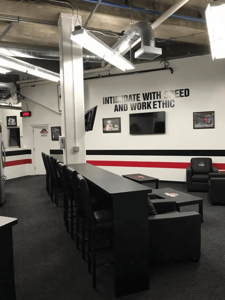 Gym interior with black tables, chairs, and wall sign reading “Integrity with speed and work ethic.”