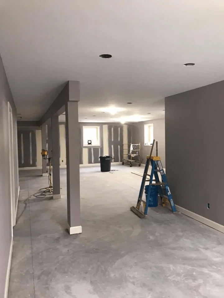 Empty unfinished interior with gray walls, concrete floors, and ladders in a construction area.
