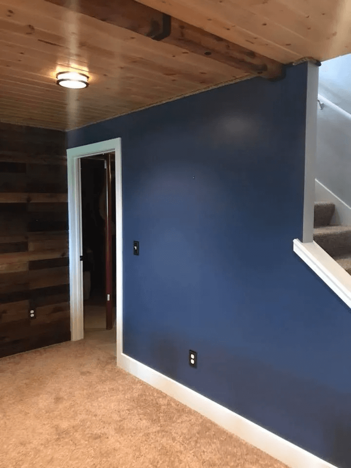 Blue accent wall in a carpeted room with wood-paneled ceiling, doorway, and staircase railing