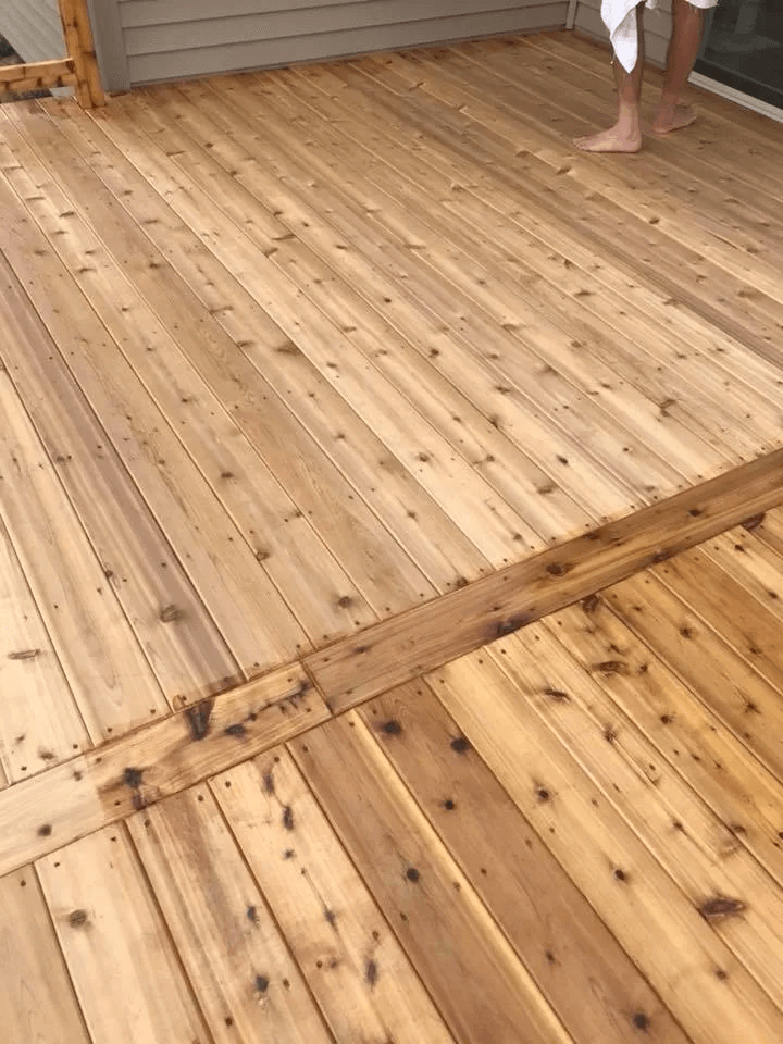 Wooden deck with visible knots and seams; two people’s lower legs visible at the top edge.