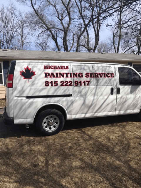 White van with “Michael’s Painting Service” sign and phone number parked outdoors under leafless trees