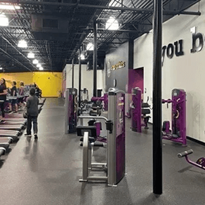 Gym interior with purple equipment, a few people, and a yellow wall in the background