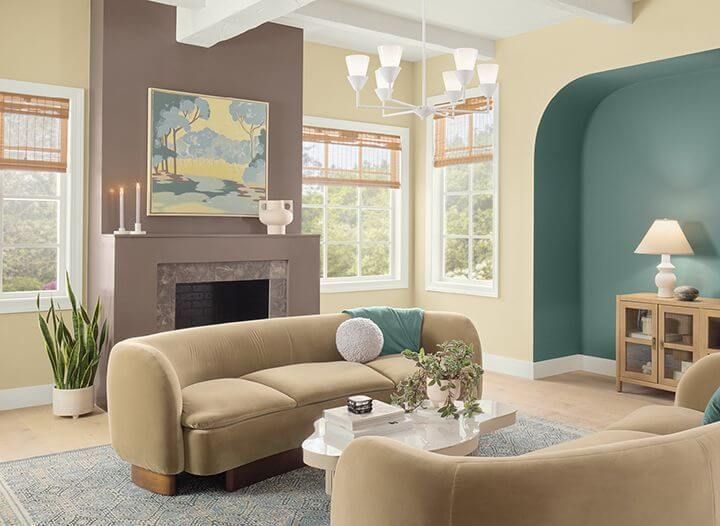 Stylish living room with dark walls, green sofa, fireplace, round table, and two armchairs by large windows