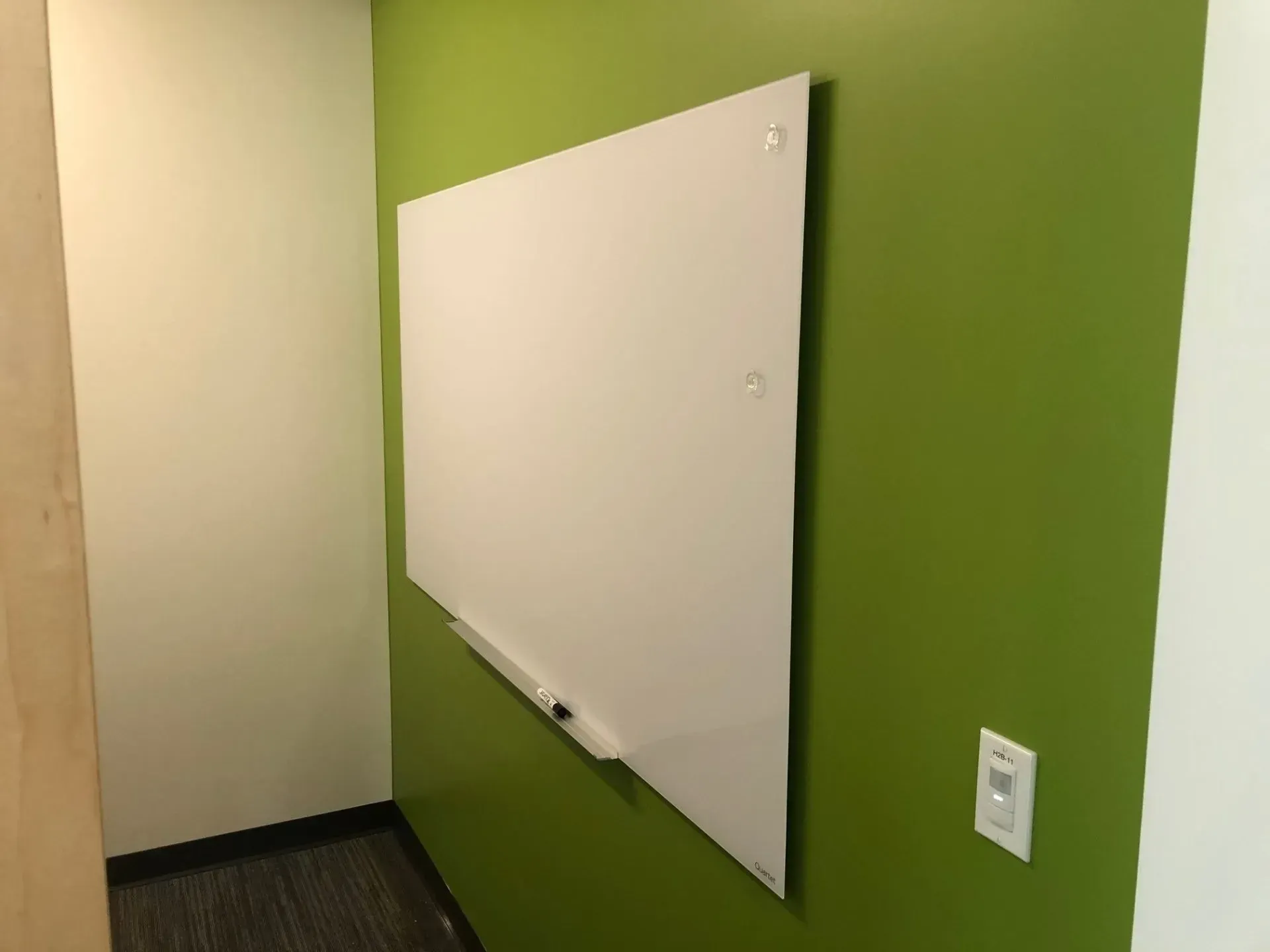 Whiteboard mounted on a green office wall in an empty room
