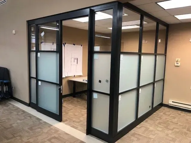 Glass-walled office meeting room with black frames and frosted panels in a beige hallway
