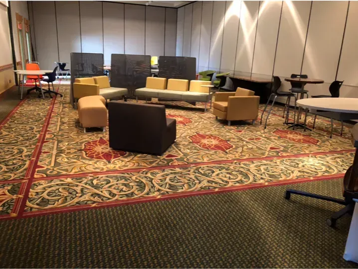 Lounge area with patterned carpet, tan sofas and chairs, and round tables in a convention hall