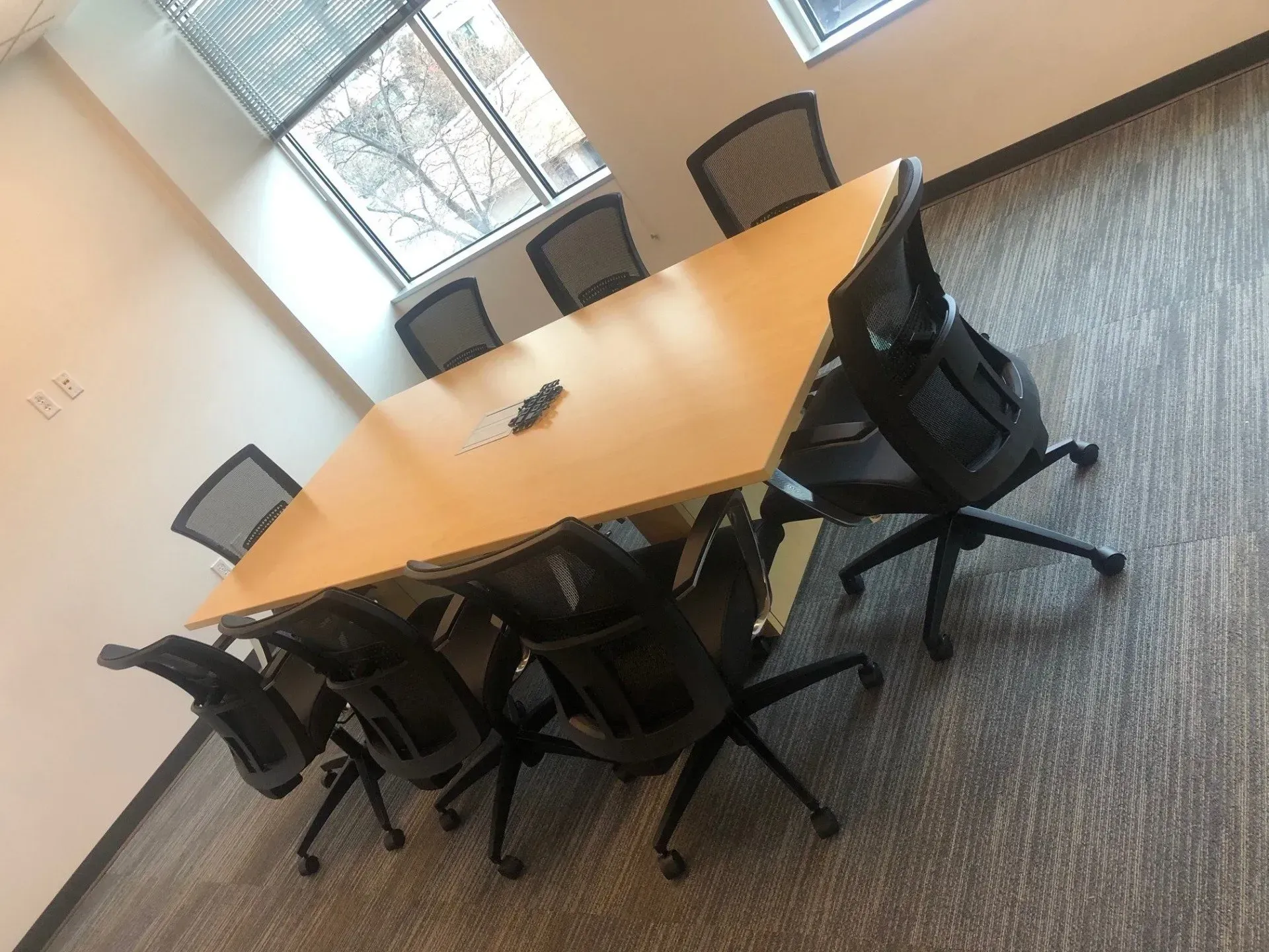 Empty conference room with a wooden table, black chairs, and carpeted floor near windows.