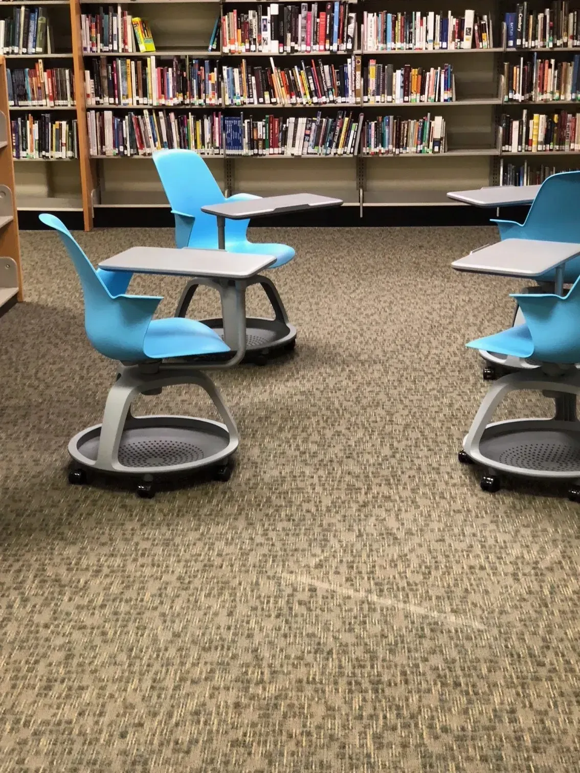 Library reading area with blue swivel chairs on carpet before bookshelves