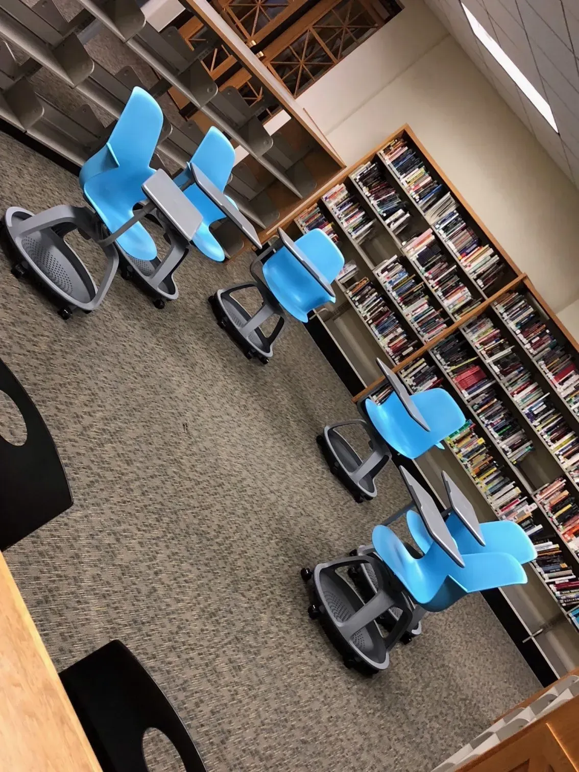 Library or classroom with blue chairs arranged on a carpeted floor, bookshelves along the wall.