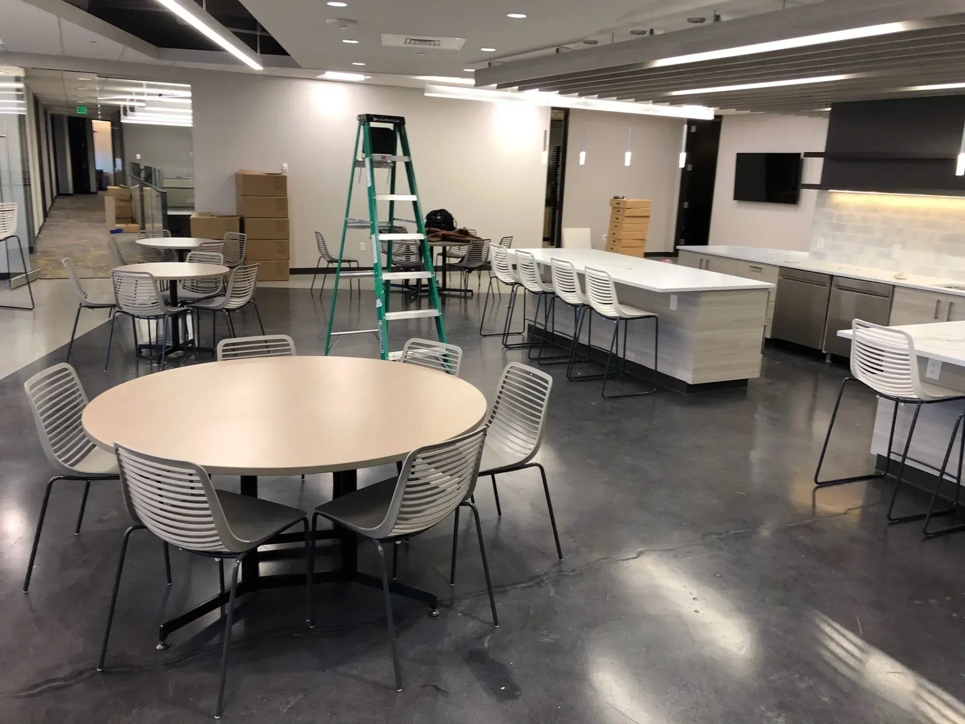 Empty cafeteria with round tables, stacked chairs, and a step ladder on a polished floor.