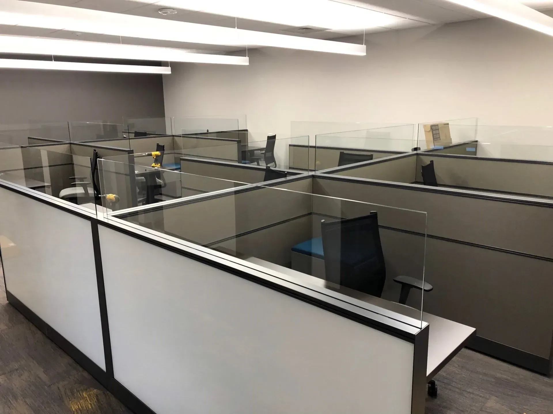 Office cubicles with empty desks and computer monitors under fluorescent lights.