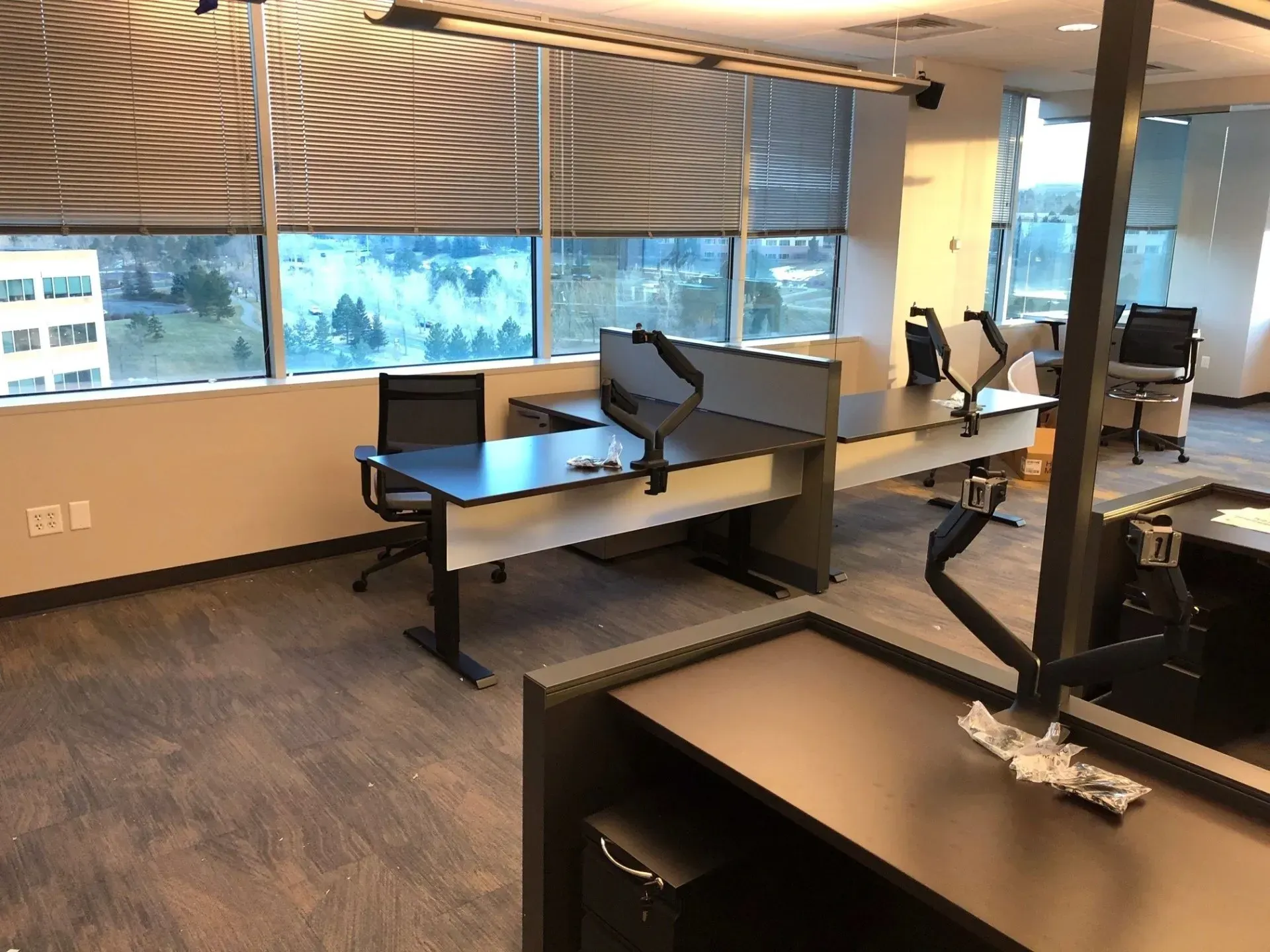 Empty office with desks, chairs, and large windows overlooking trees and buildings