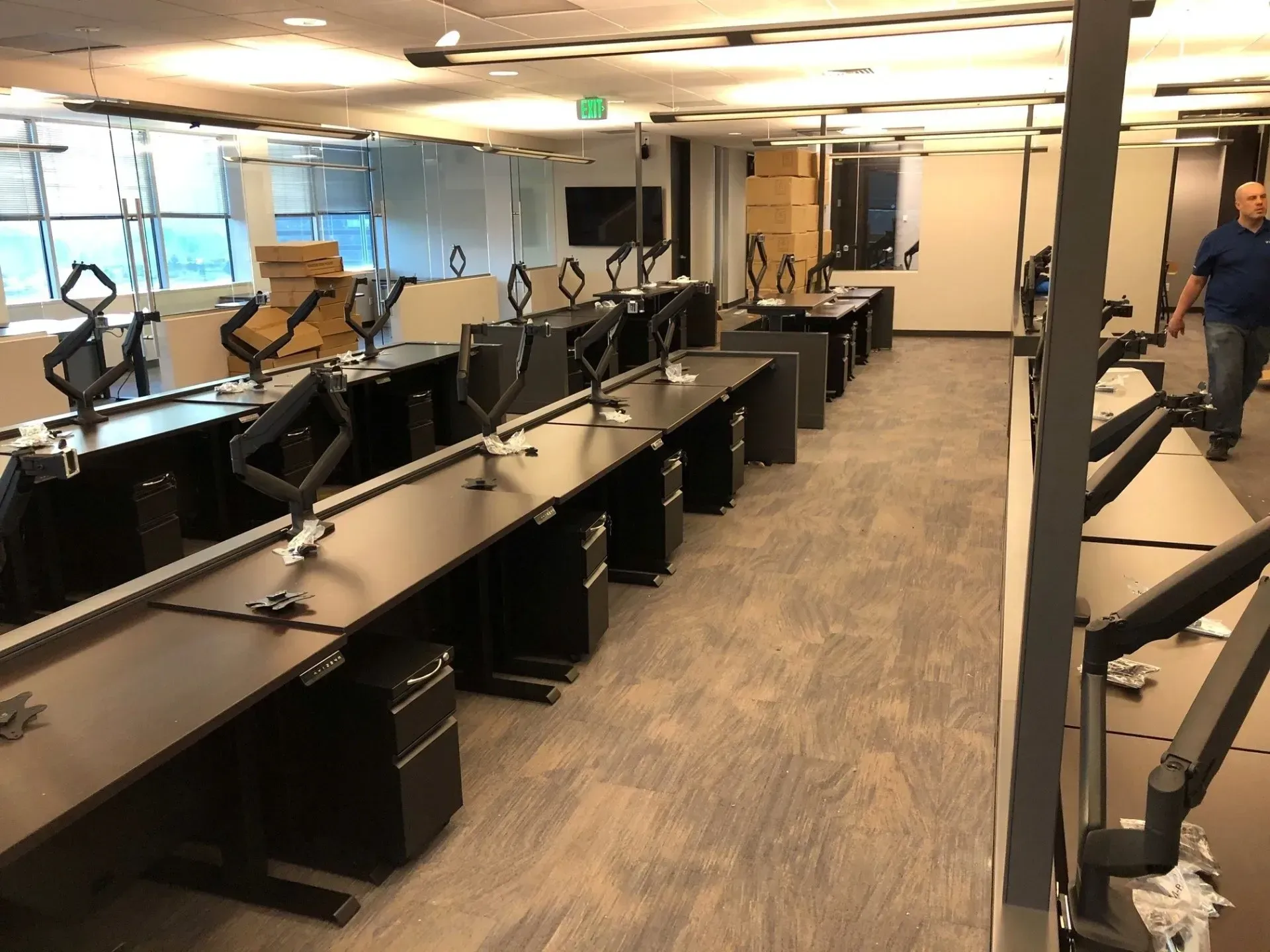 Large open office with rows of black desks and chairs, carpeted floor, and one person walking at the back.