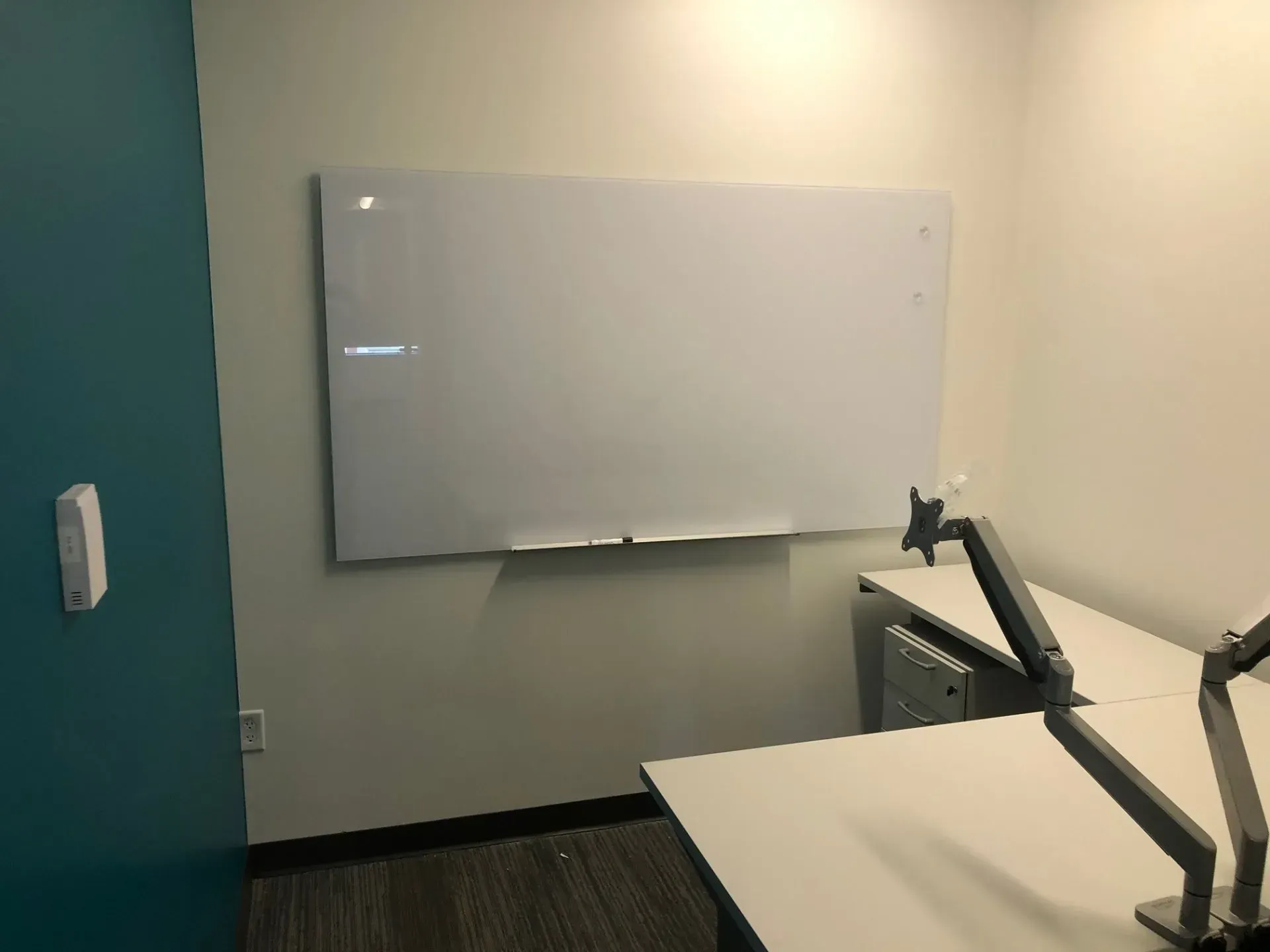 Small meeting room with whiteboard, teal door, and a desk with monitor and chair.