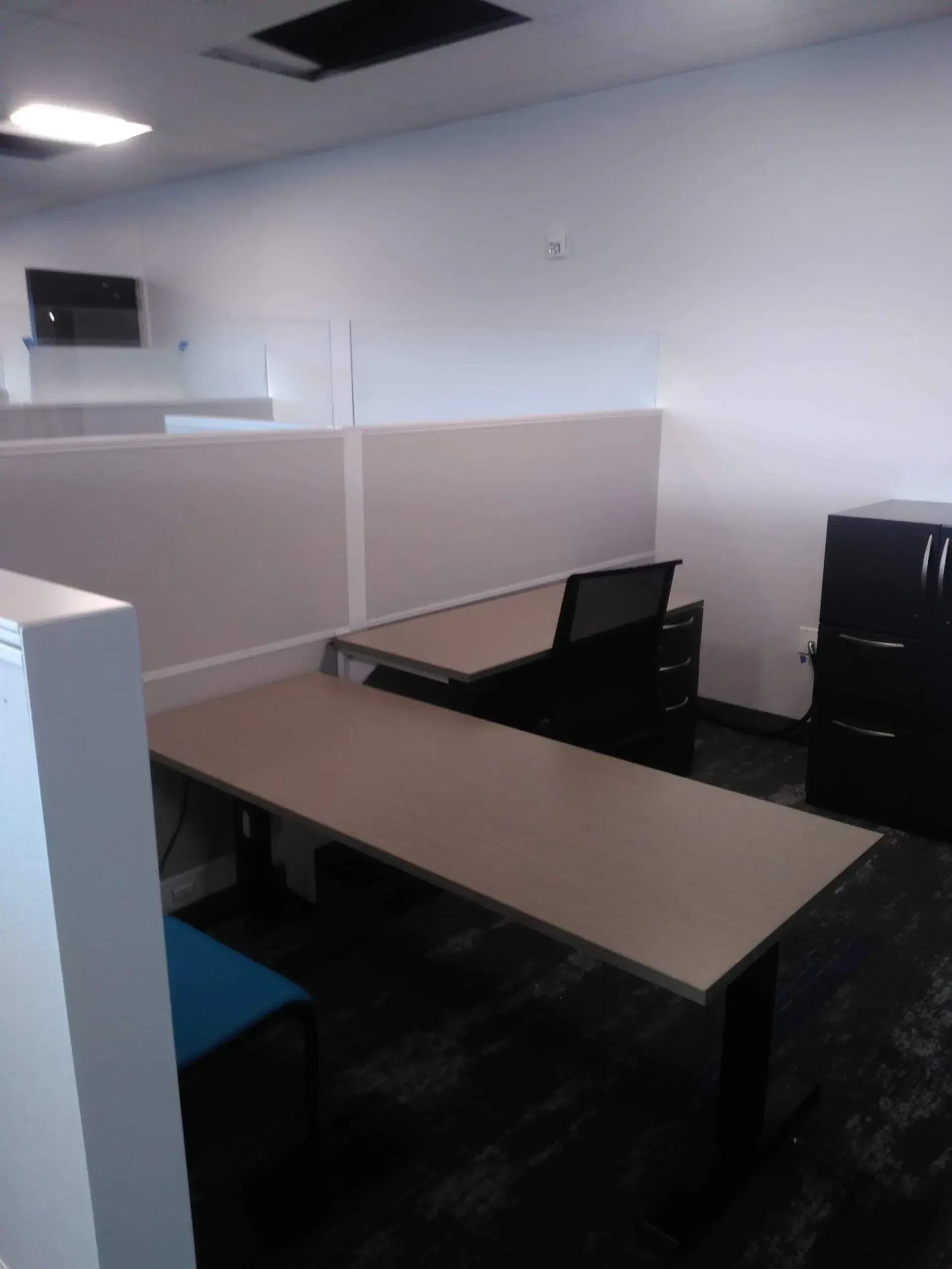 Empty office cubicle with beige desks, black chairs, and gray partition walls