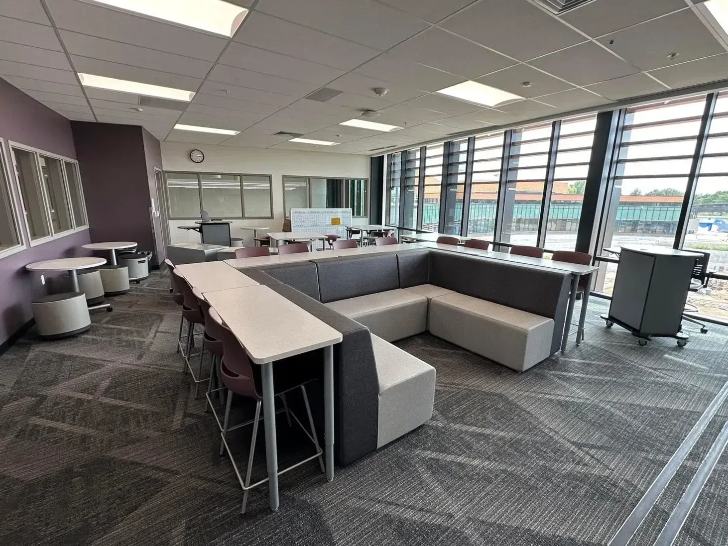 Modern office lounge with gray seating, tables, and large windows overlooking a parking lot