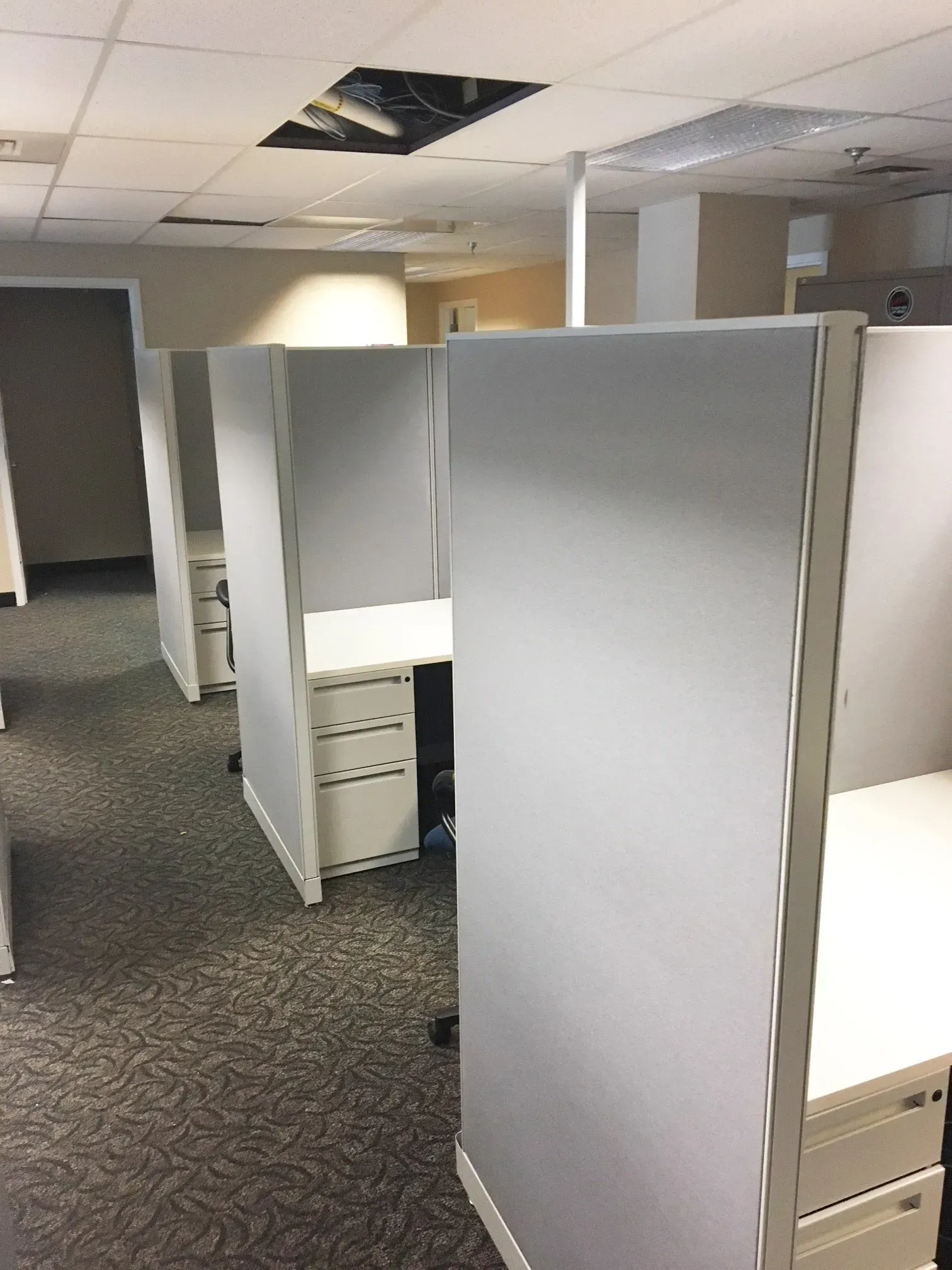 Empty office cubicles with gray partitions and overhead fluorescent lighting