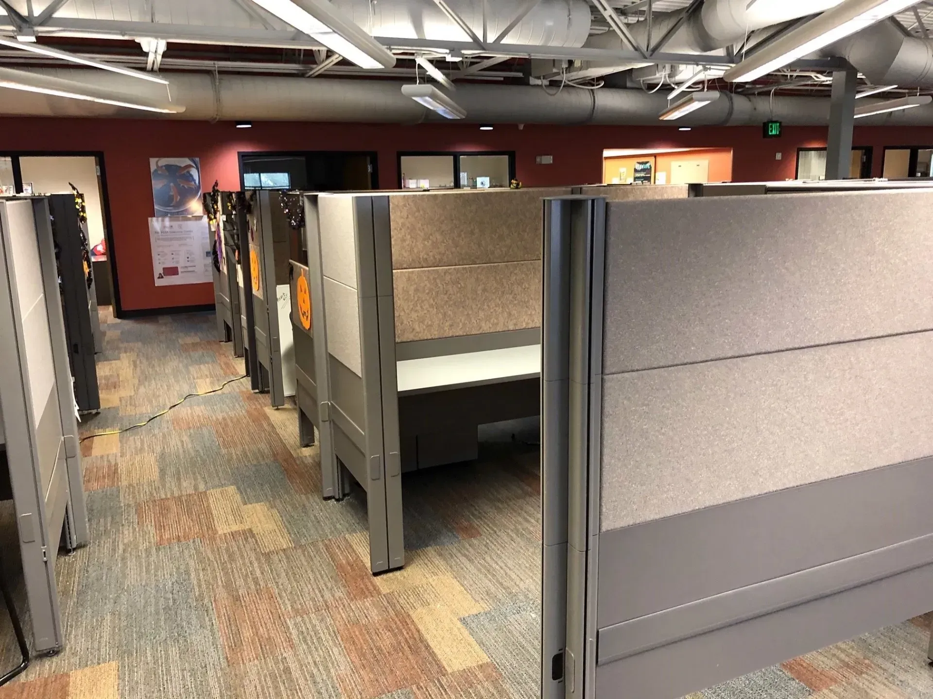 Office cubicle rows with gray partitions and carpeted floor in a workspace corridor